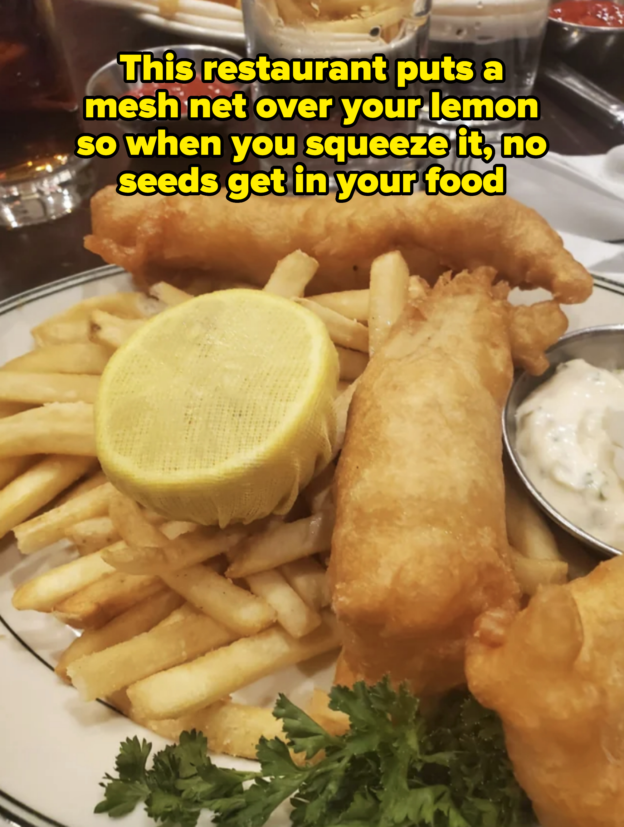 Plate with two pieces of fried fish and chips, garnished with parsley and lemon. Tartar sauce on the side
