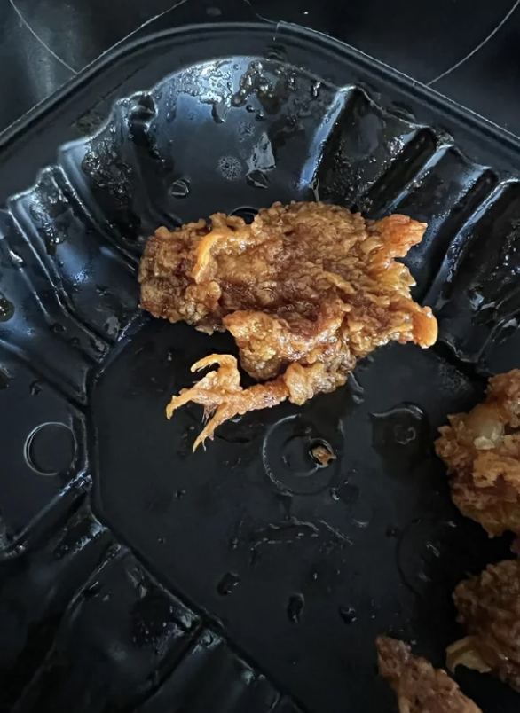 A single piece of fried chicken on a black plate with visible grease
