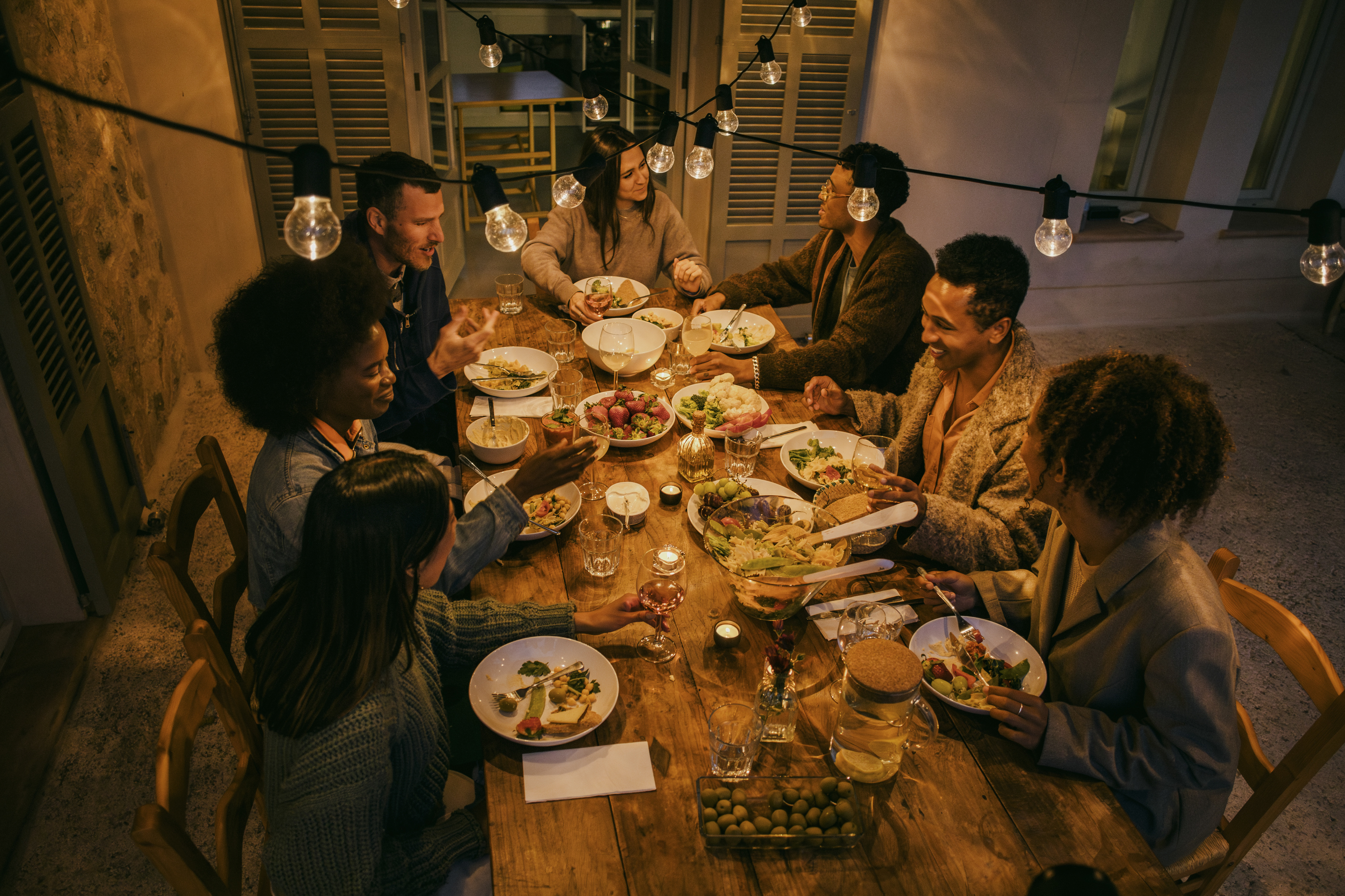 Group of people enjoying a meal together at a table under hanging lights