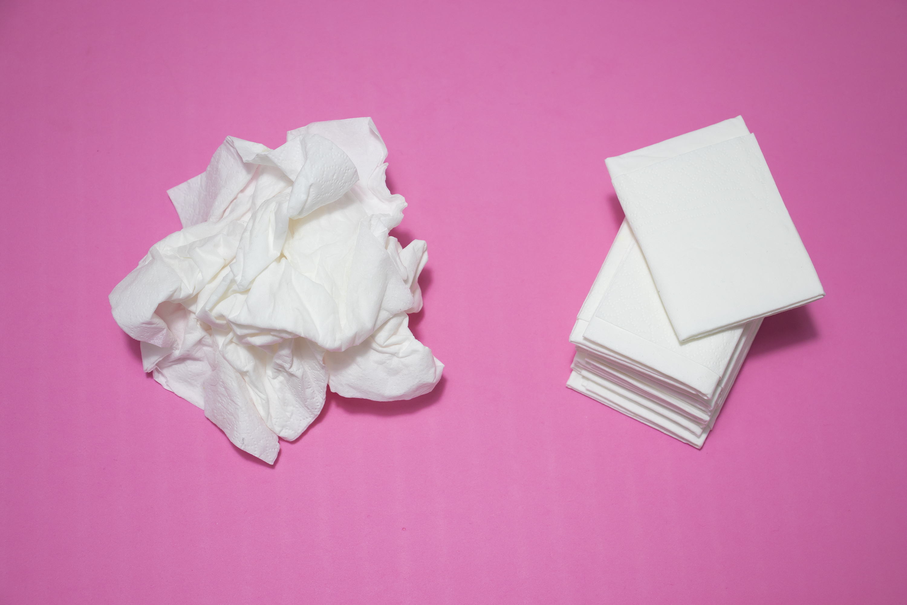 A pile of used tissues next to a new pack on a pink surface