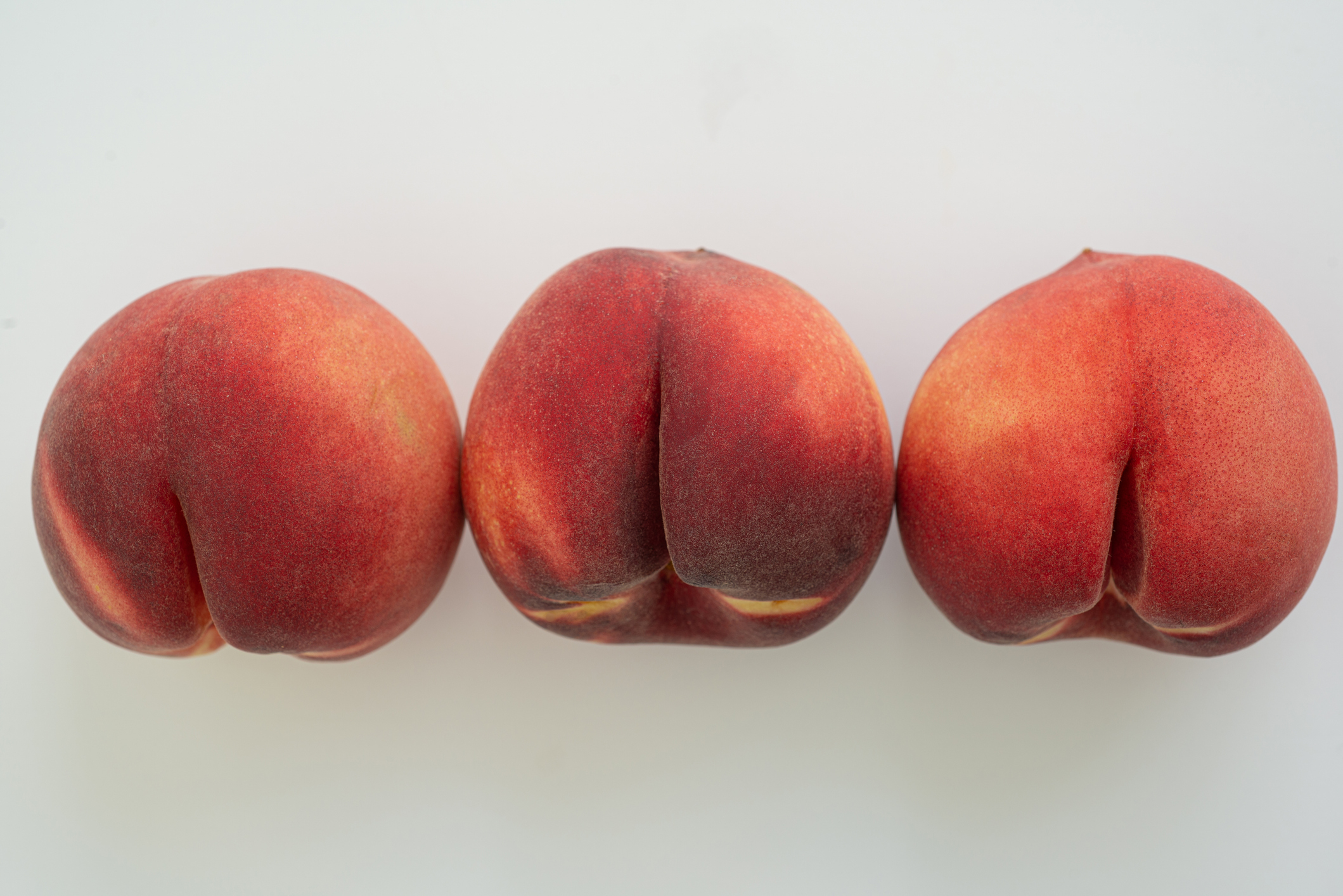 Three peaches in a row resembling human buttocks, suggesting a playful take on sensuality