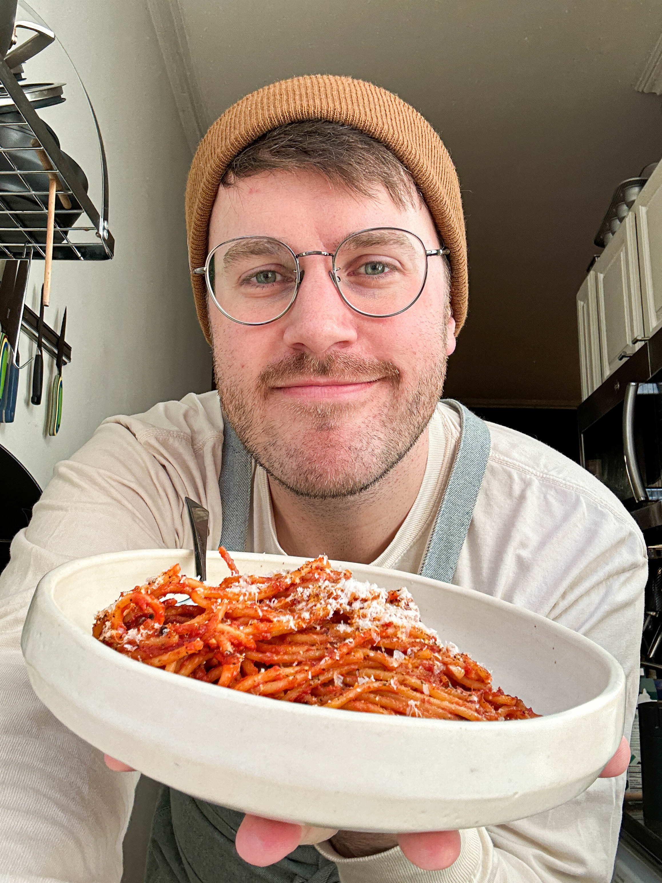 Person holding a bowl of spaghetti, smiling at the camera