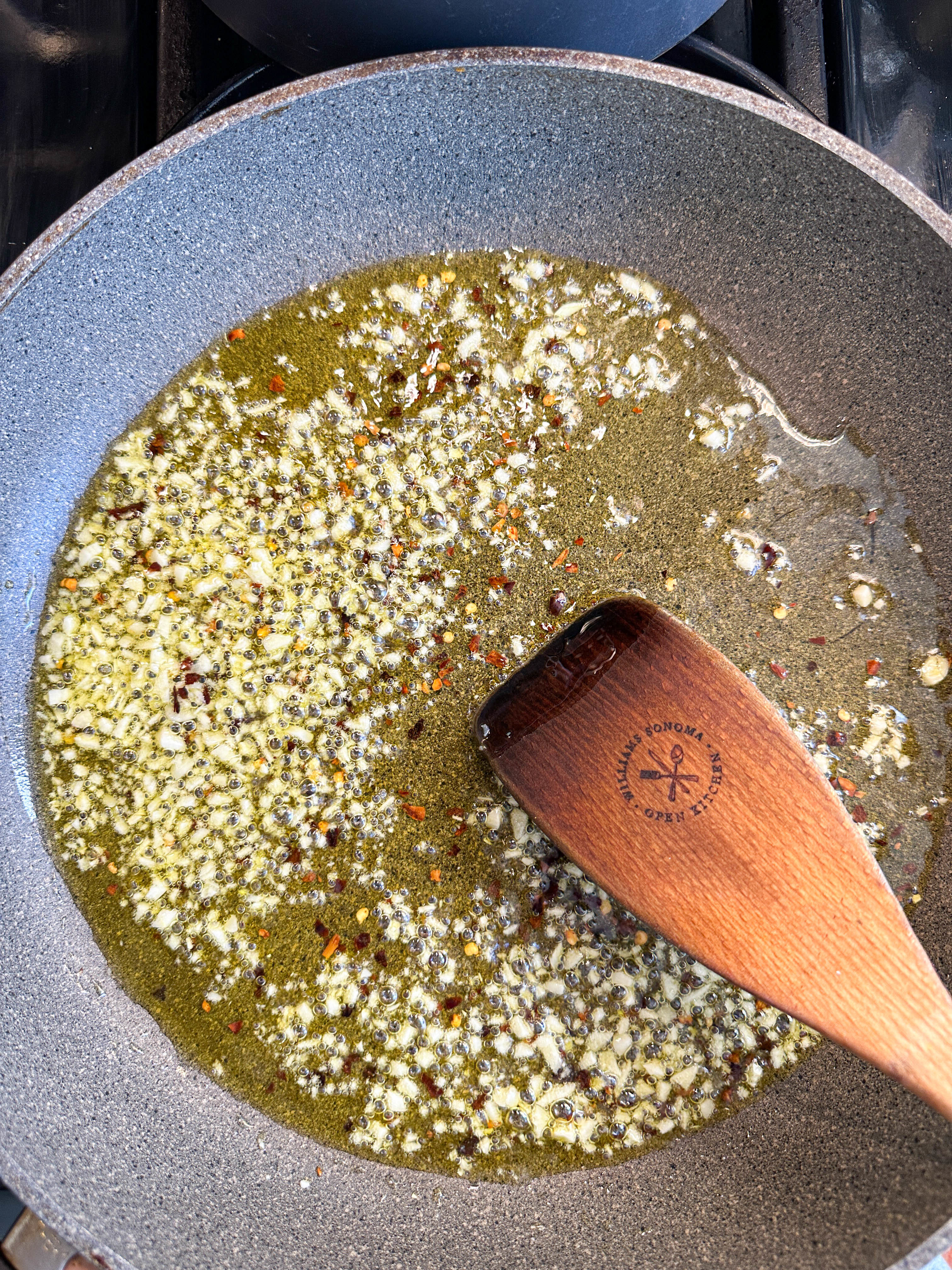 A wooden spatula rests in a pan with oil and spices being cooked on a stove