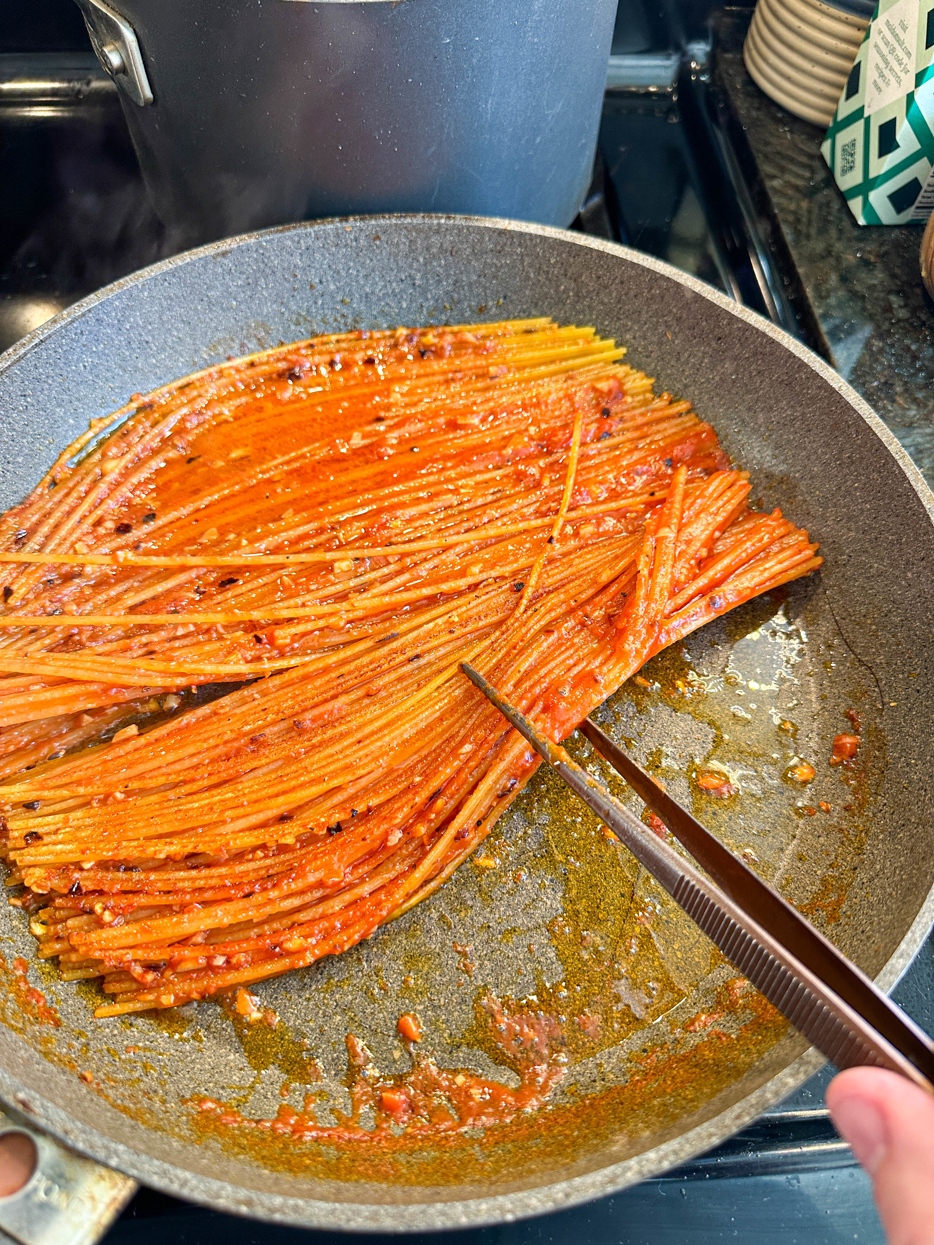 Spaghetti being flipped in a pan with tomato sauce, hand holding tongs