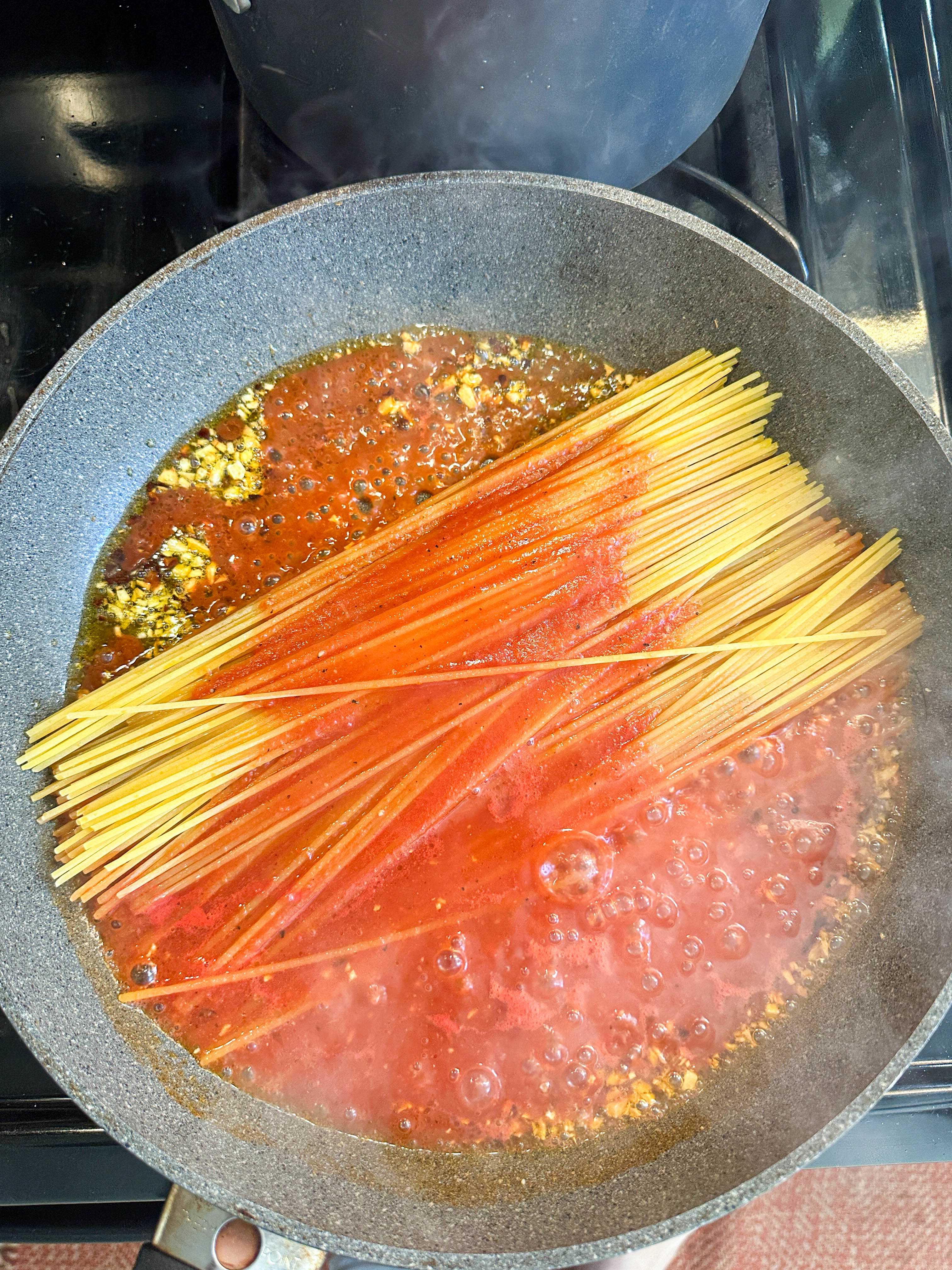 Spaghetti noodles half-submerged in boiling tomato sauce