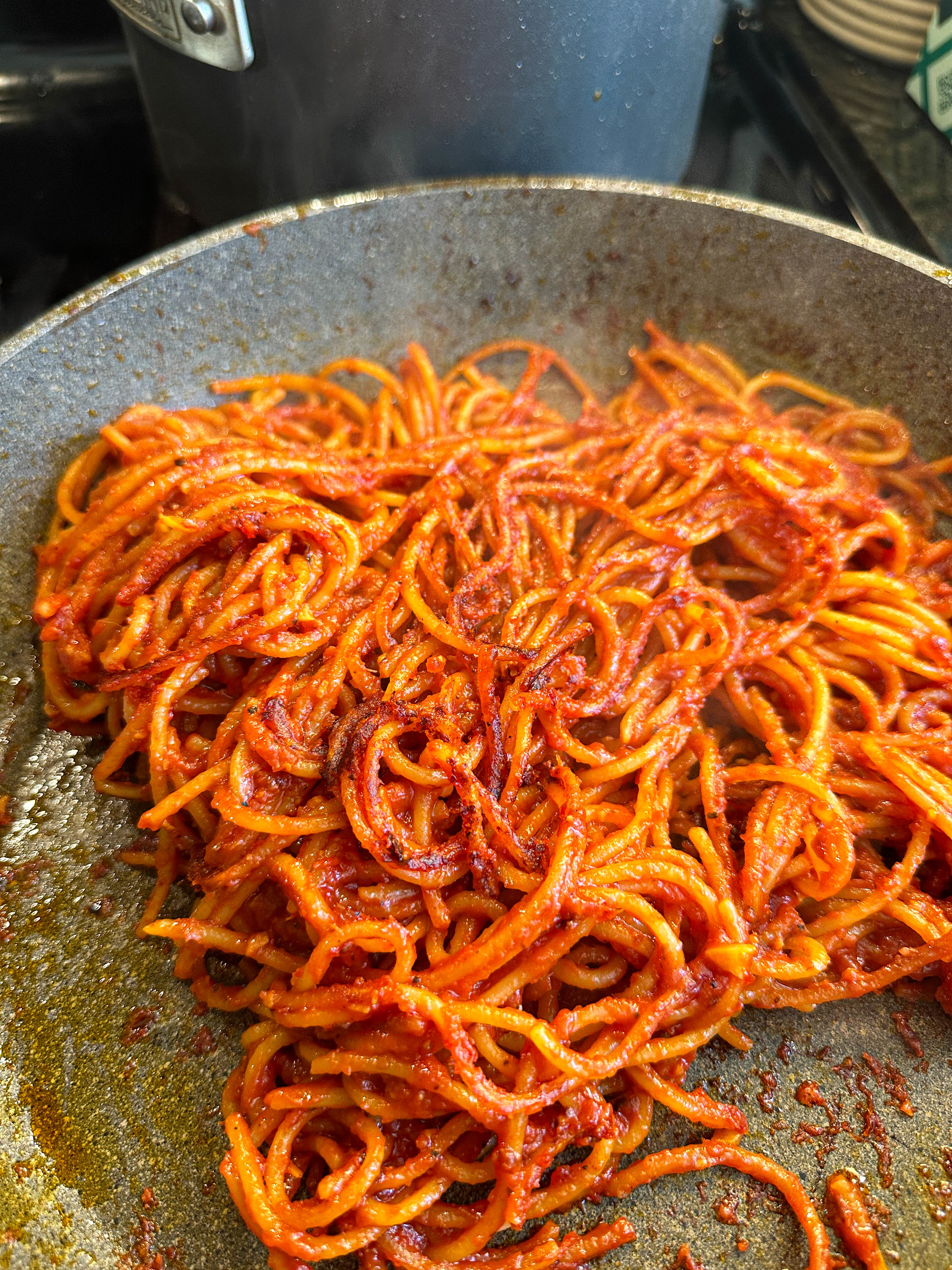 A pan of spaghetti with charred red sauce being cooked on a stove