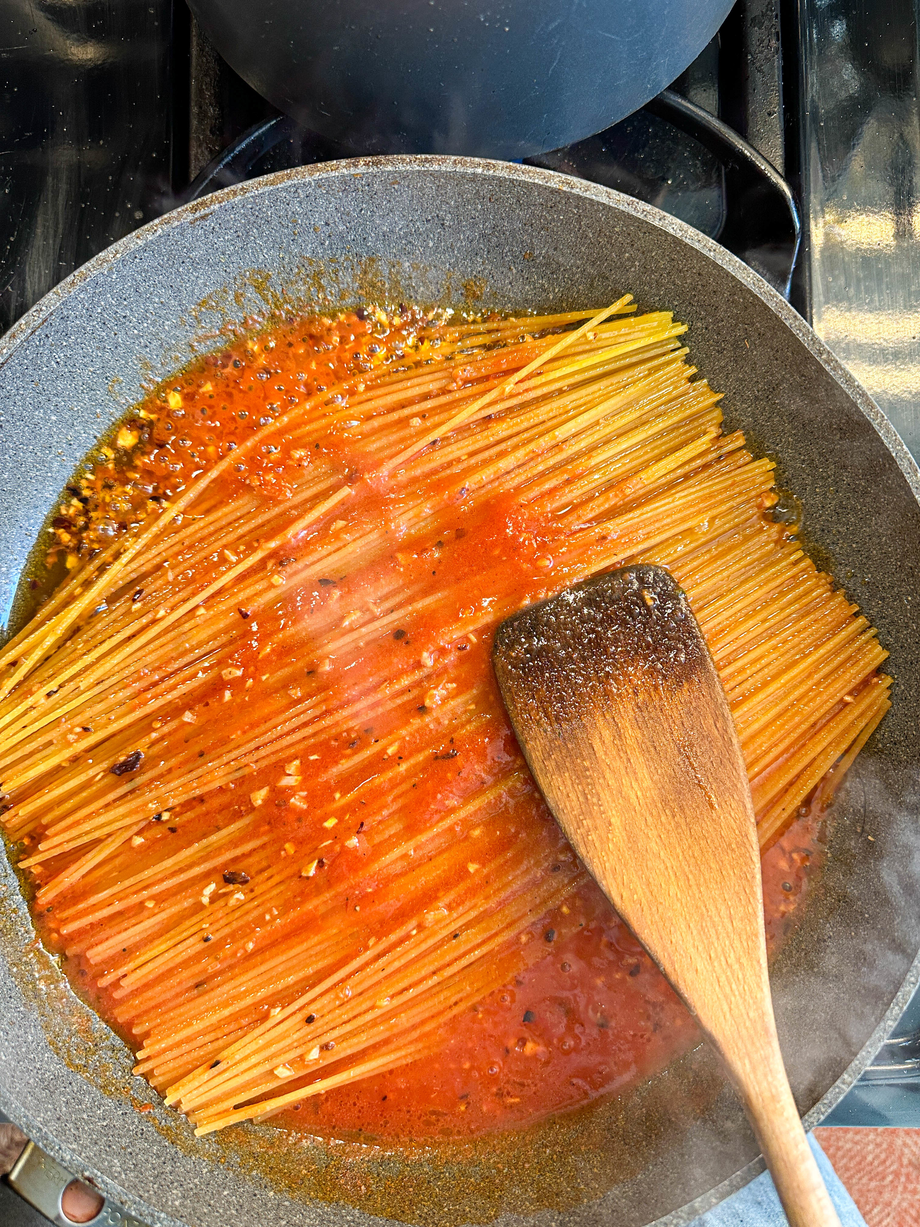 Uncooked spaghetti with sauce in a pan with a wooden spoon