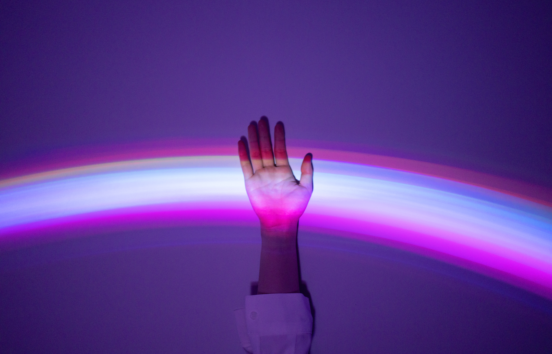 Hand intercepting a blurred light spectrum in a dark room, symbolizing connection or touch