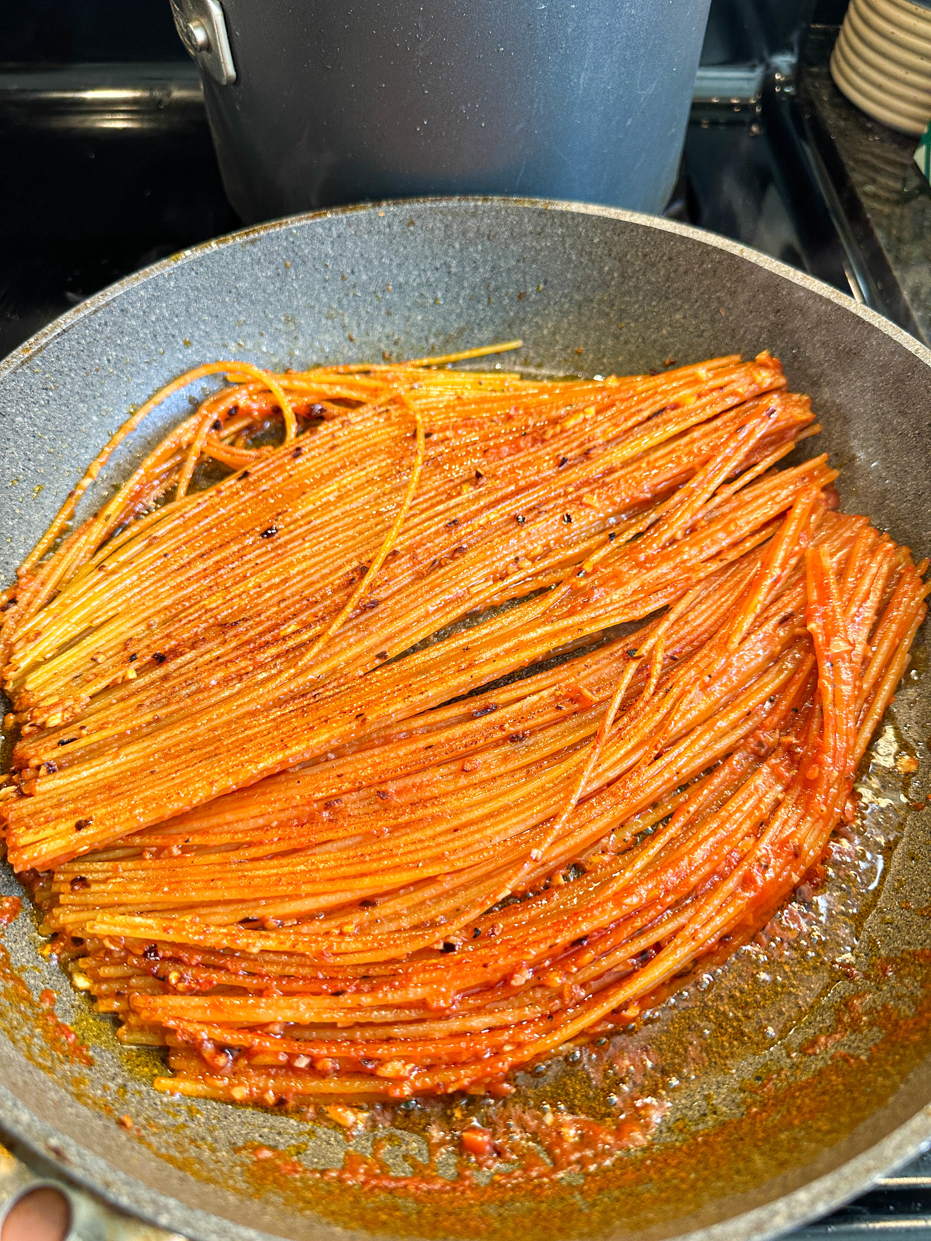 Spaghetti being cooked in a pan with tomato sauce