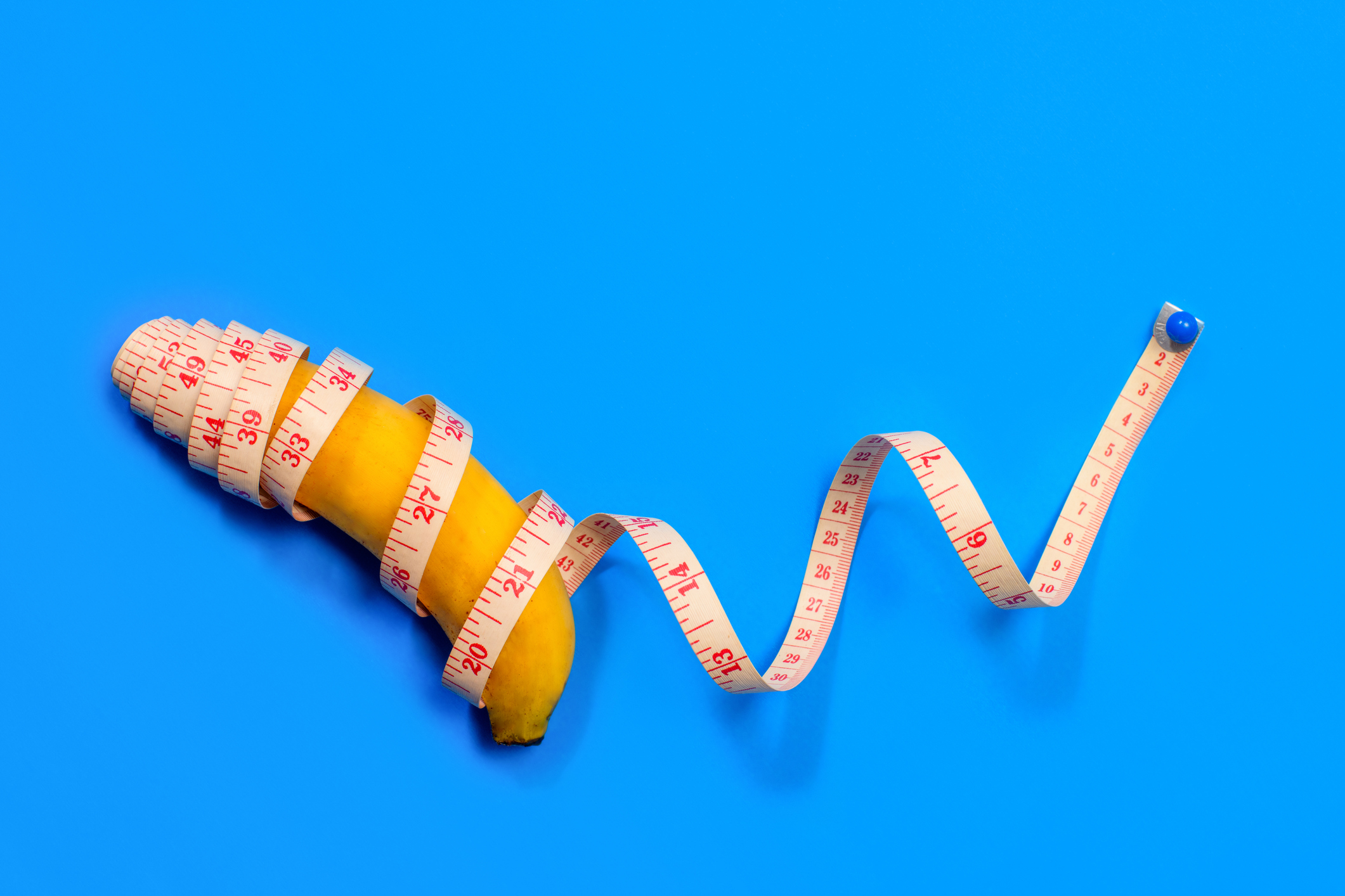 Banana wrapped with a measuring tape on a blue background, implying body image themes related to sex and love