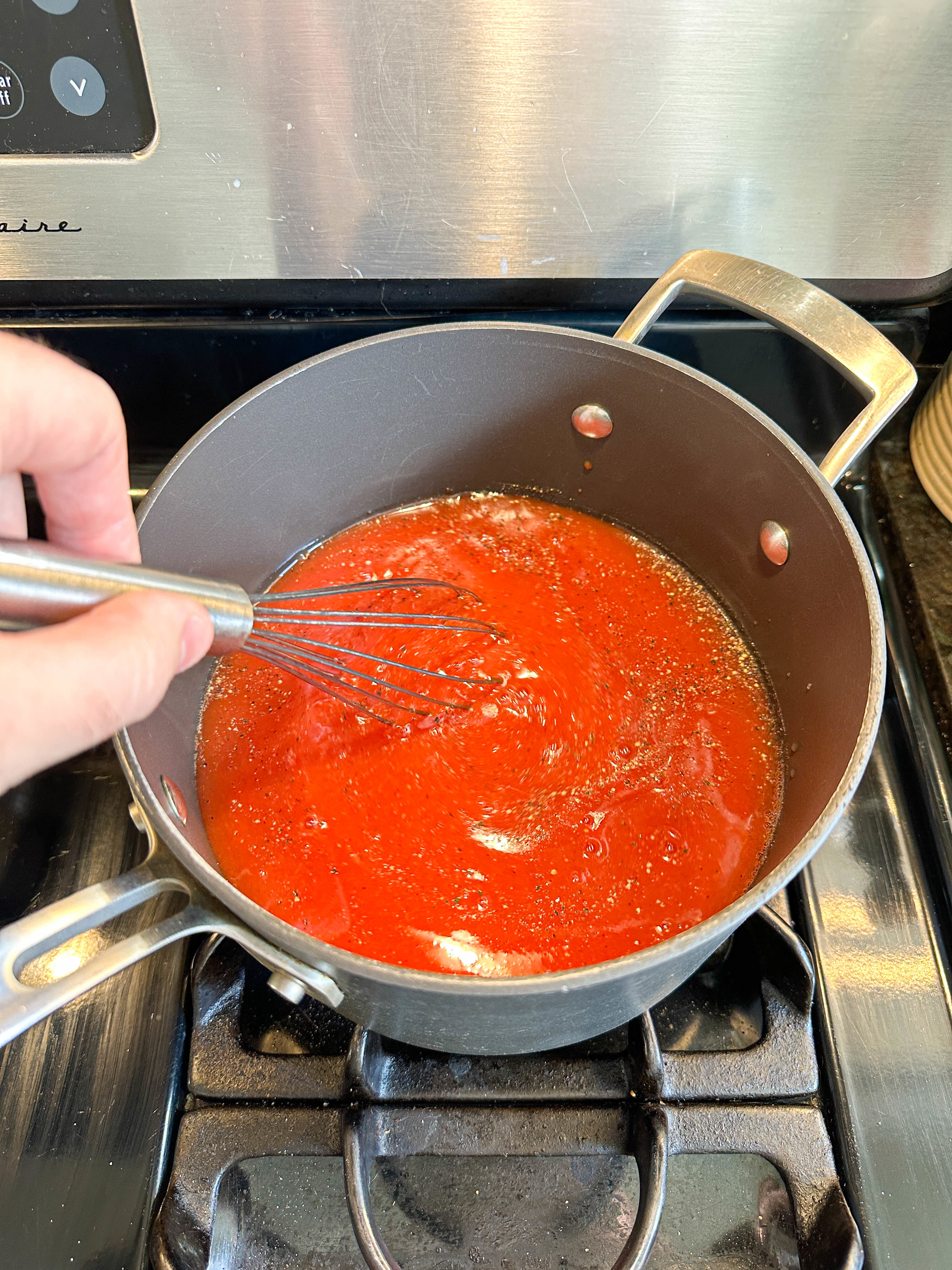 Hand whisking tomato sauce in a pot on a stove