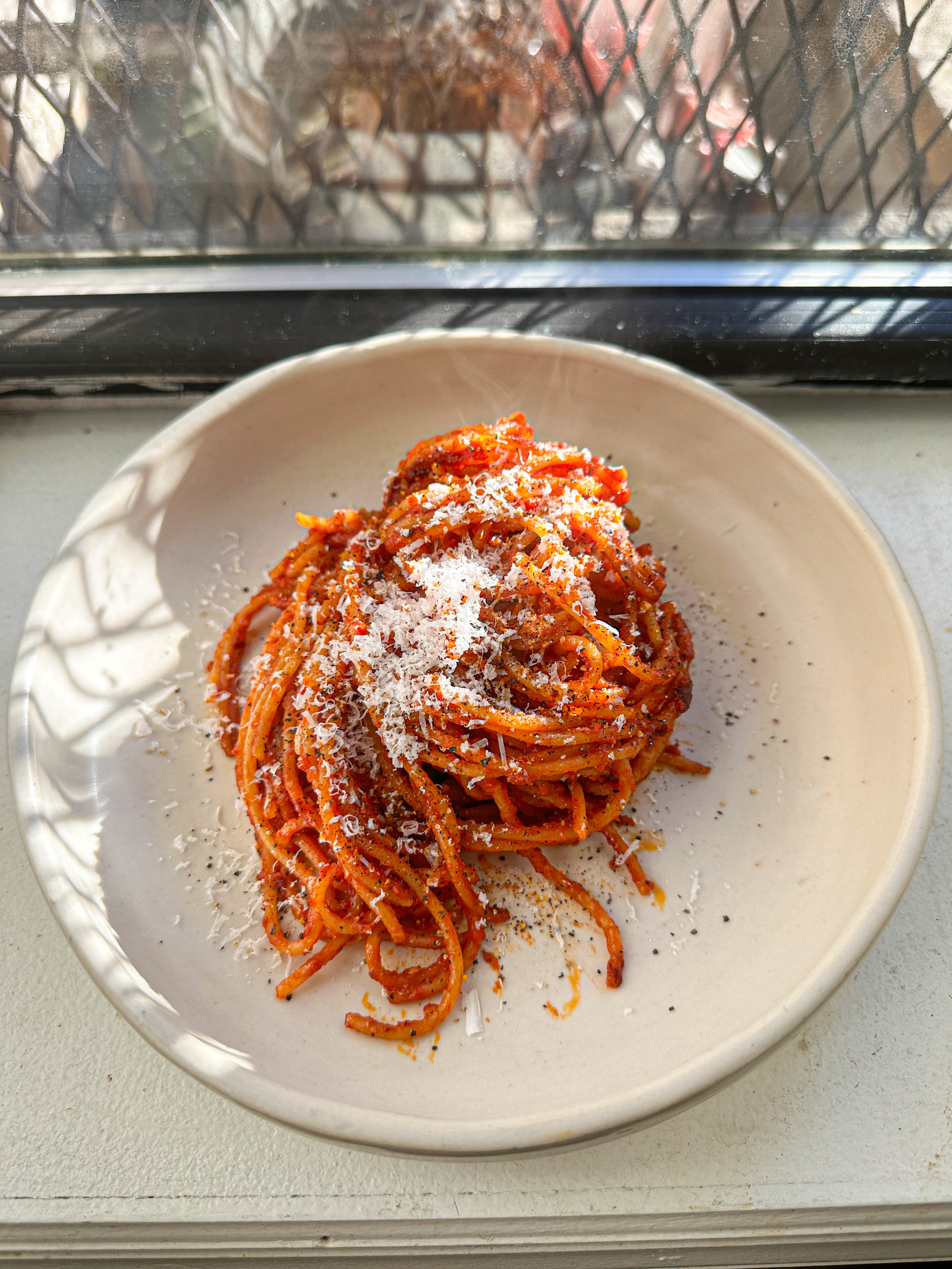 A plate of spaghetti with tomato sauce and grated cheese on a windowsill