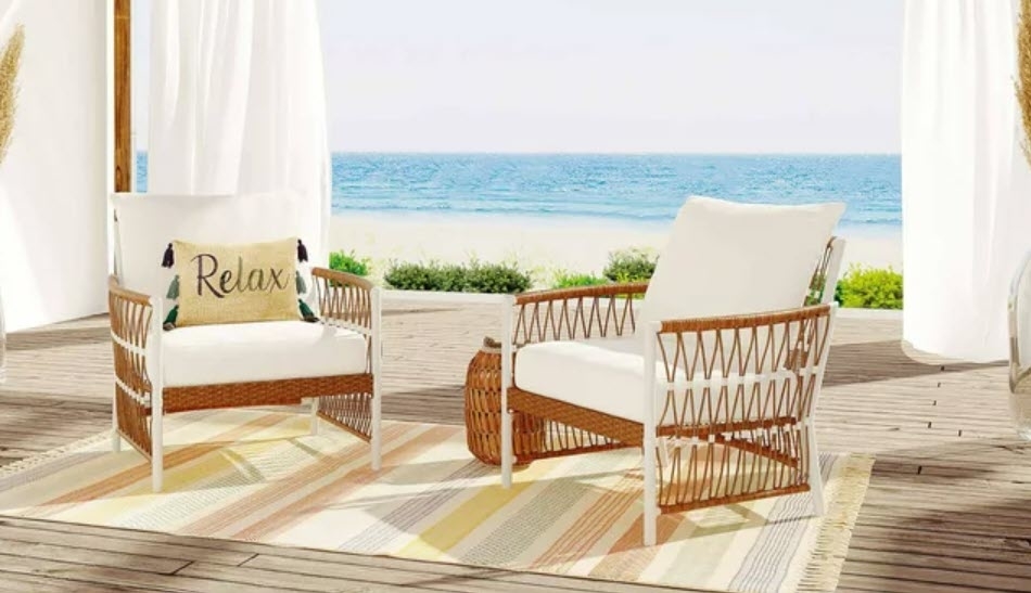 Two woven chairs with cushions on a deck by the beach, one with a &quot;Relax&quot; pillow. No persons present