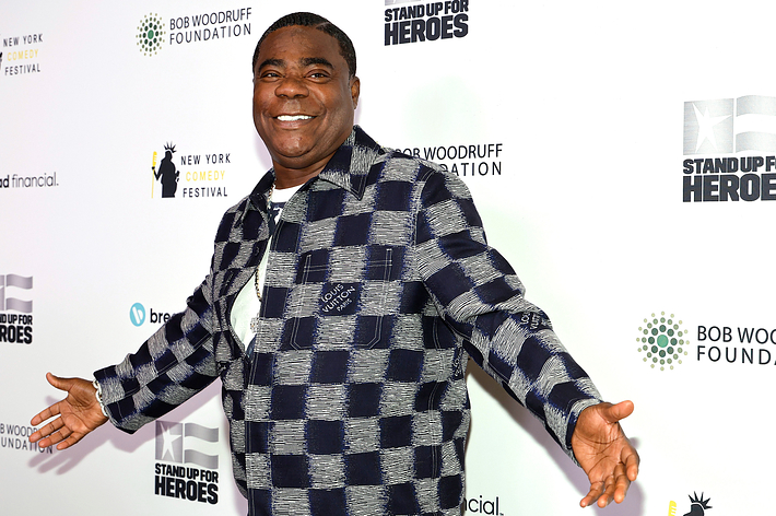 Tracy Morgan in a checkered jacket and pants standing with arms open wide at a Stand Up for Heroes event