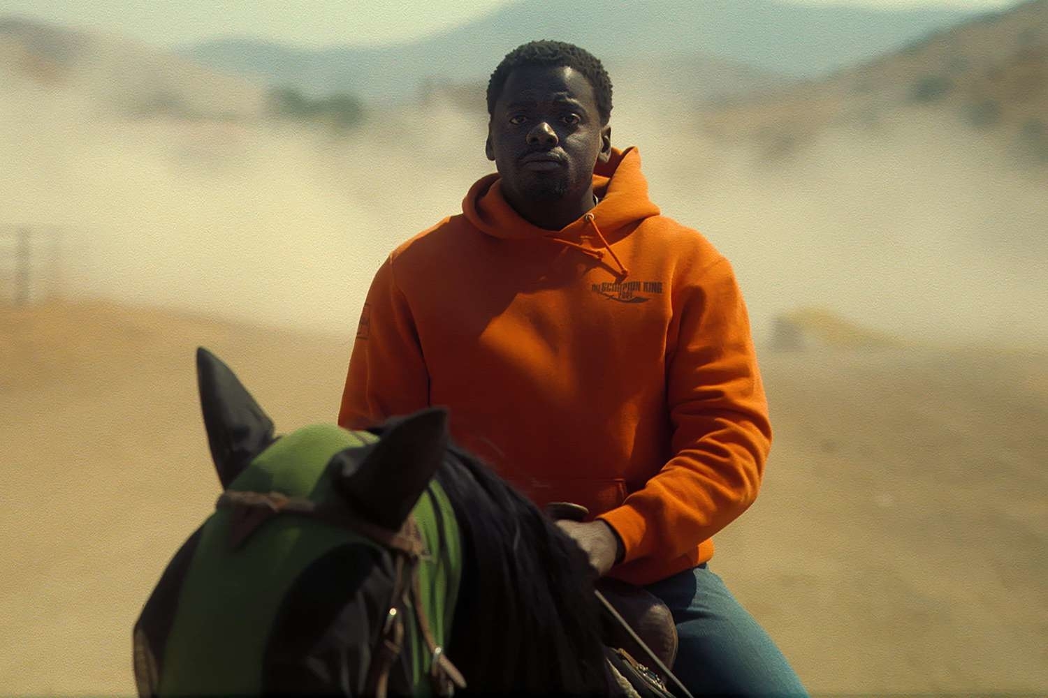 Daniel Kaluuya on horseback wearing an orange hoodie with a foggy landscape in the background