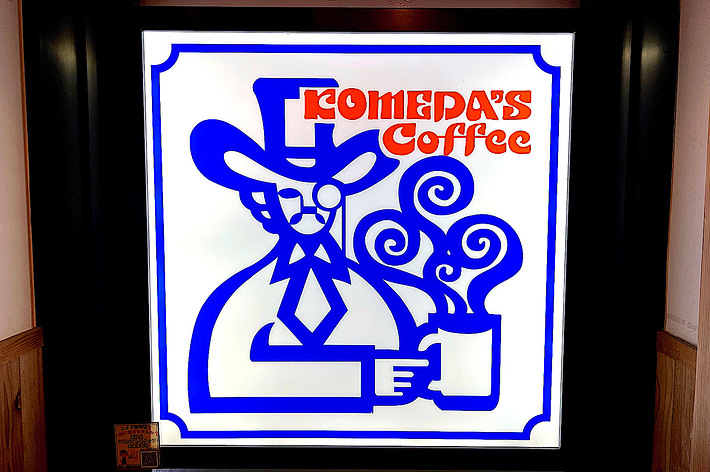 Sign with a stylized design featuring a figure in a hat holding a steaming cup, text reads &ldquo;ROMEDA&rsquo;S Coffee.&quot;