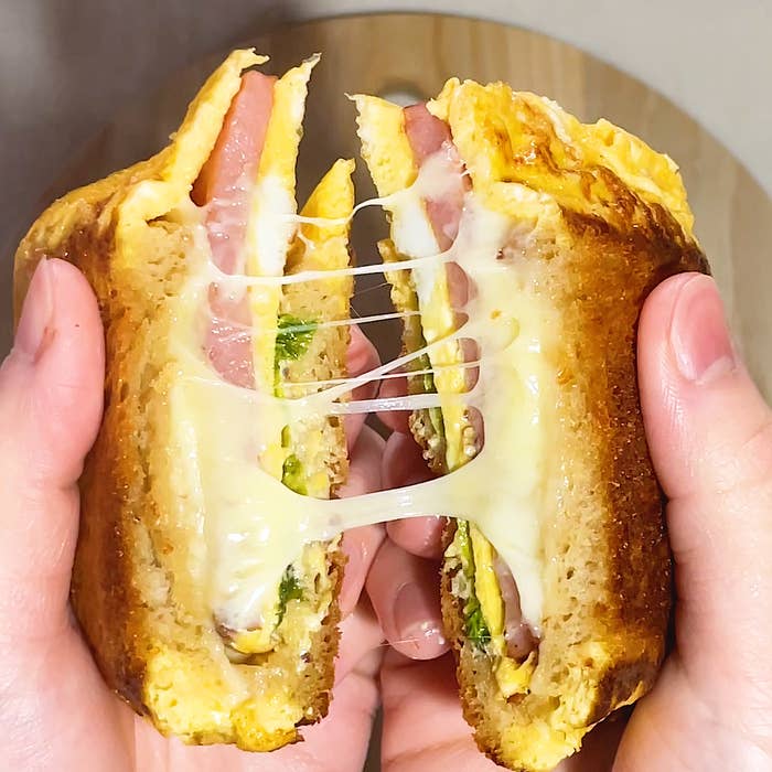 手で持ったサンドイッチが中央で割れ、チーズが引き伸びる様子