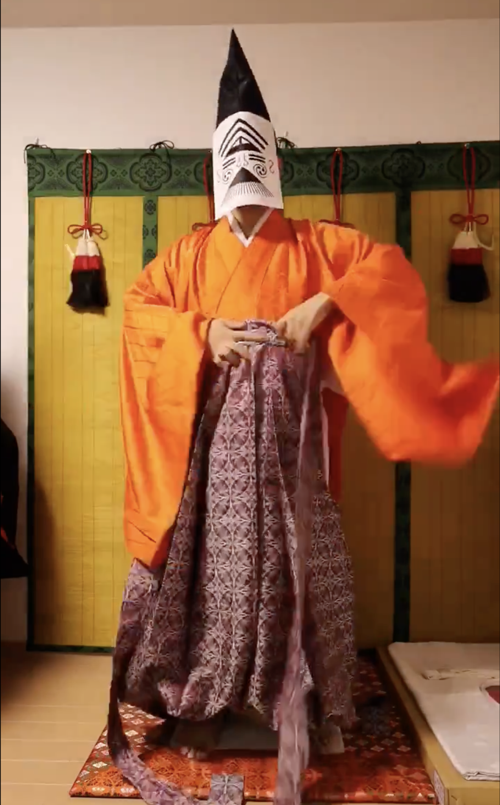 着物を着る人、鬼の面をかぶり、背景には日本の伝統的な飾りがあります。