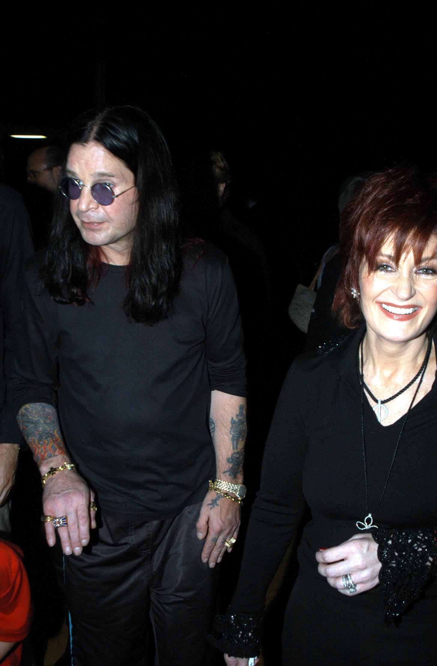 Ozzy Osbourne and Sharon Osbourne holding hands at an event, Ozzy in a long-sleeved shirt and Sharon in a embellished outfit