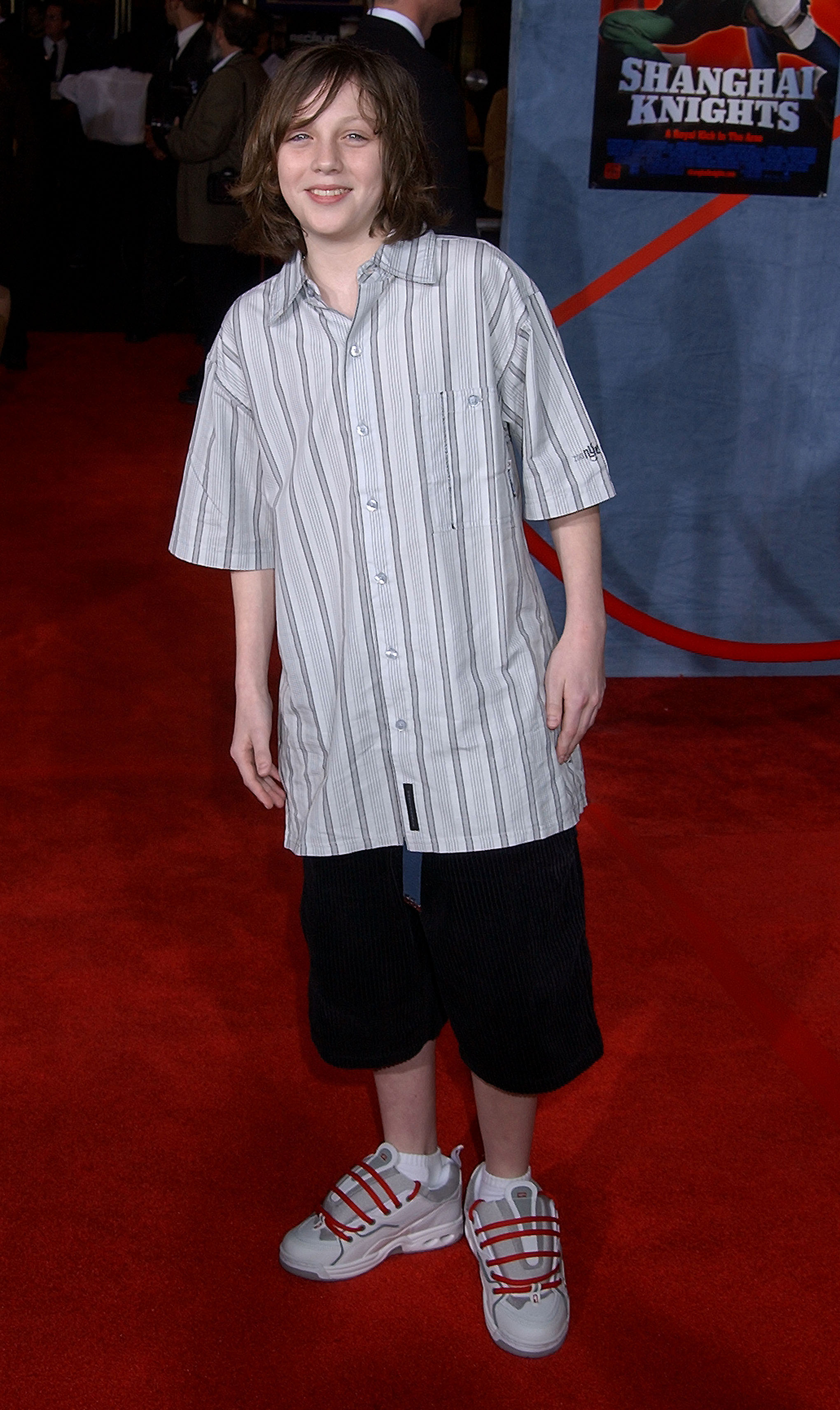 Aaron as a young boy in a striped shirt and dark shorts on the red carpet, smiling