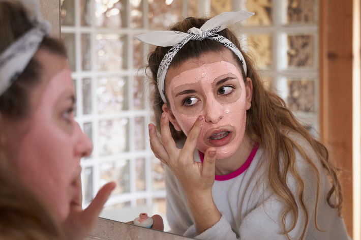 女性が鏡を見ながら顔にスキンケアのマスクを塗っている。