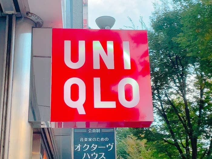 UNIQLO store sign with brand name in bold letters, viewed from street level with trees in the background