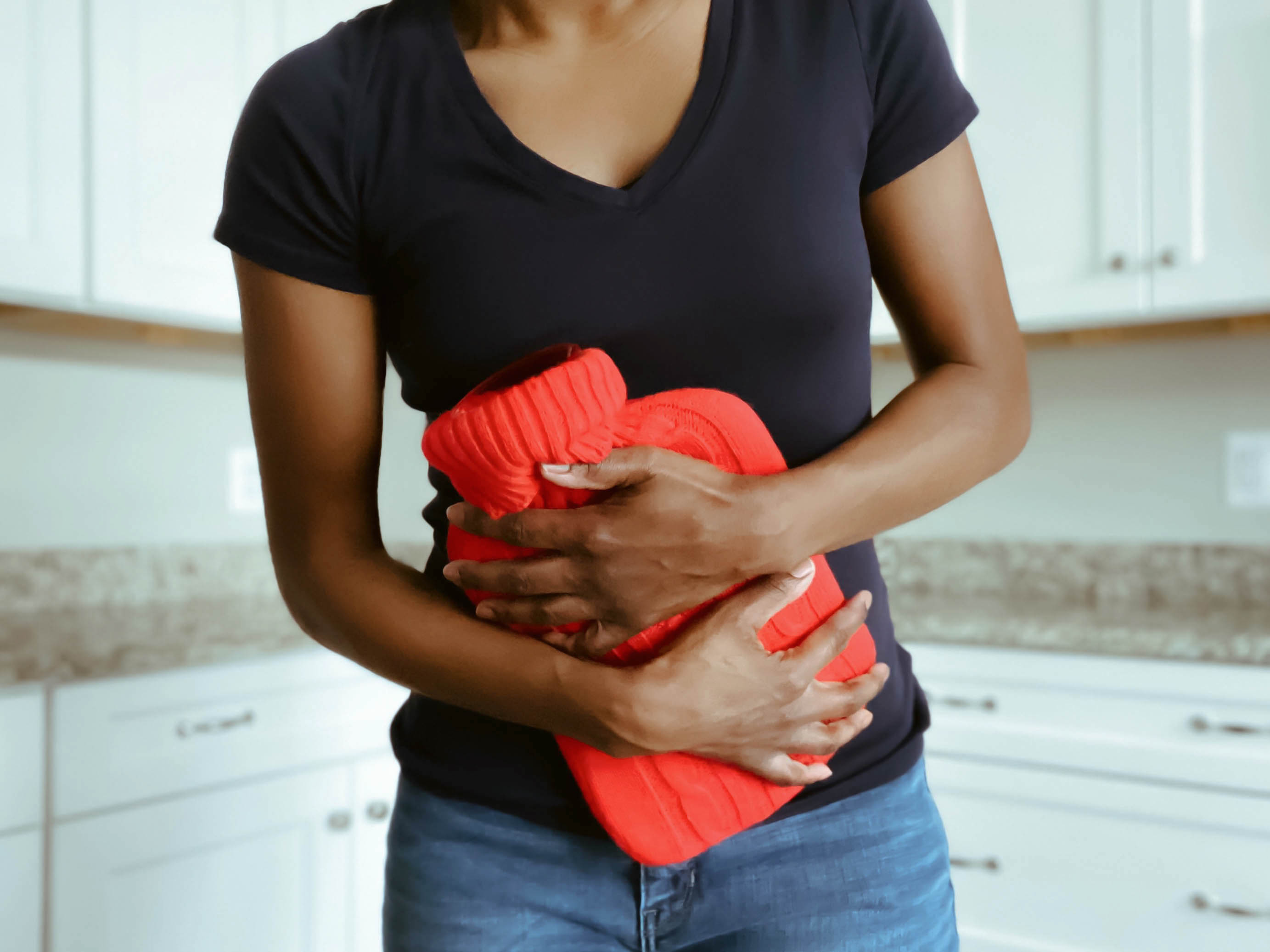 Person holding a bright red knitted item to their stomach in a kitchen