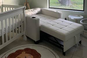 Nursery room with a crib, sofa, rug, and a window with blinds