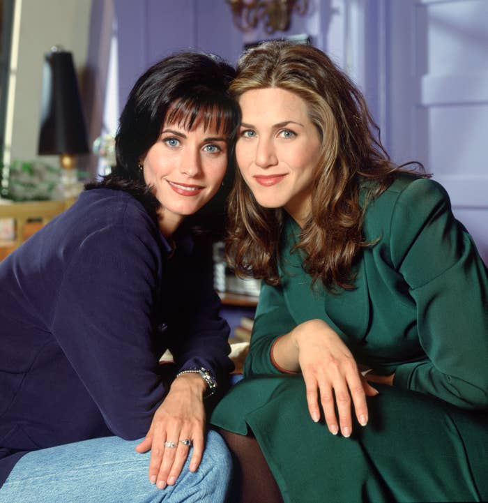 Monica and Rachel from Friends sit smiling, dressed in casual tops and jeans