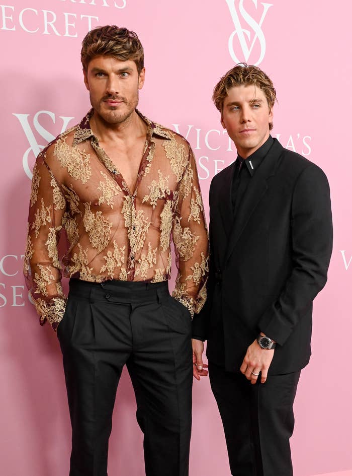 Chris in a sheer lace shirt and Lukas in a black suit at an event