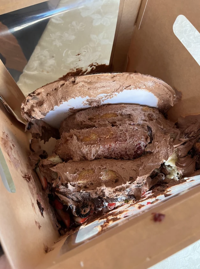Open box with a partially eaten chocolate-covered dessert with layers and filling