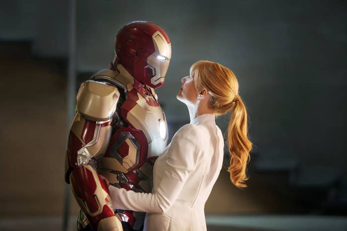 Iron Man in armor facing Gwyneth with hair styled in a ponytail, wearing a business suit, in a close moment