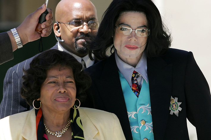 Michael Jackson in a dark suit with a decorative armband, walking alongside two individuals