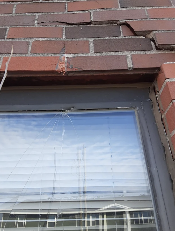 A cracked window set in a brick wall, showing signs of damage at the top left corner