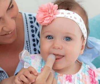 Woman and baby with a headband; baby getting teeth cleaned with finger tool
