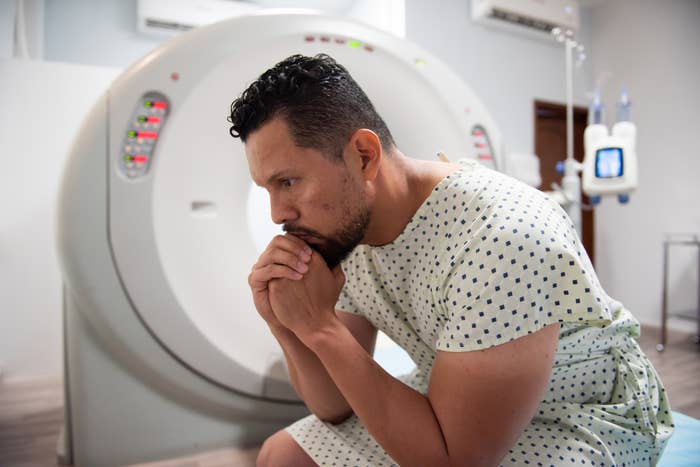 Person in a hospital gown sits contemplatively beside an MRI machine