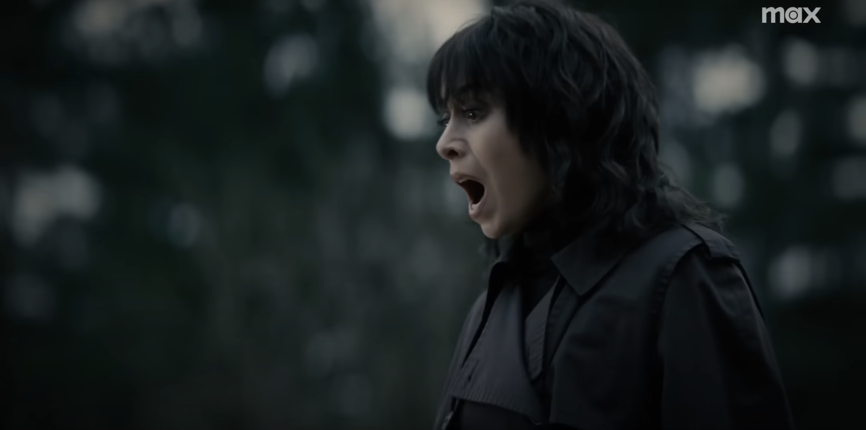Character in a dark outfit with an open mouth, expressing shock or fear, in a forest setting
