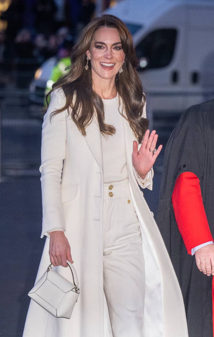 Kate in a stylish coat over a matching ensemble, waving with a smile