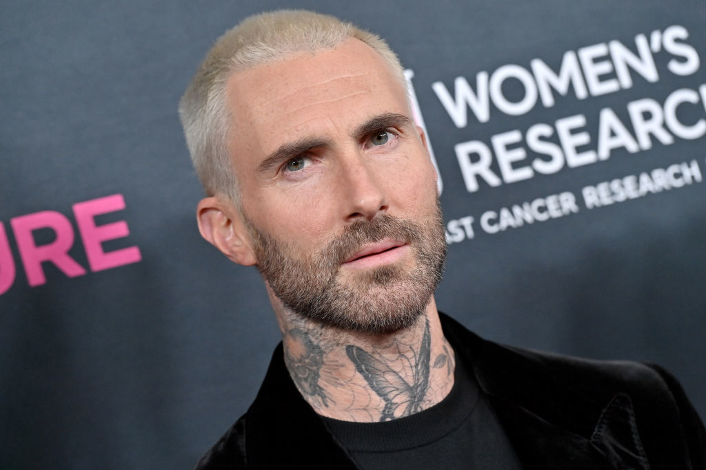 Man with buzzed hair and tattoos on neck wearing a dark suit at an event