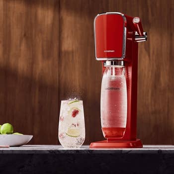 SodaStream sparkling water maker on a countertop with a glass of carbonated drink beside it
