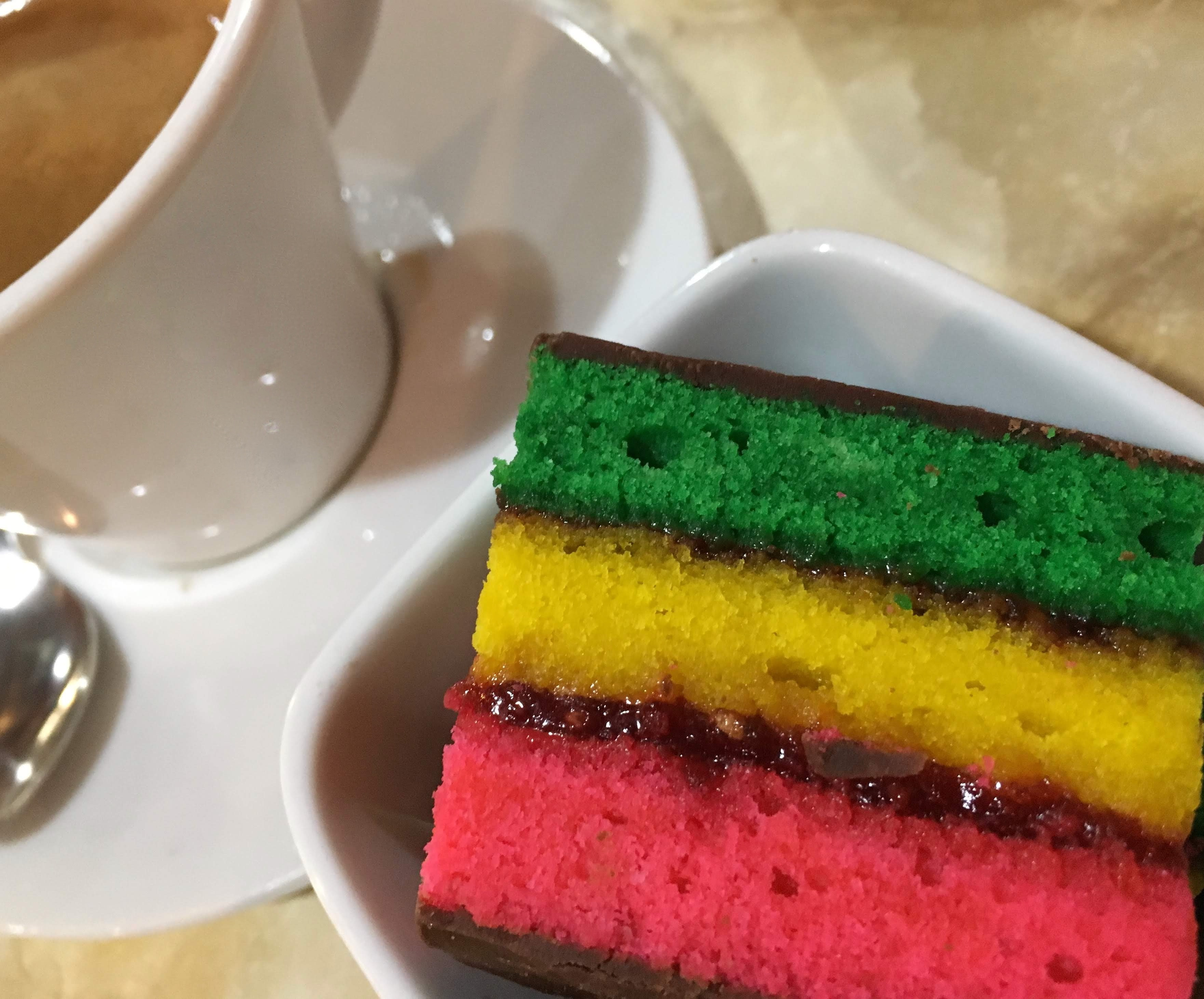 Slice of rainbow cake next to a toppled coffee cup on a saucer