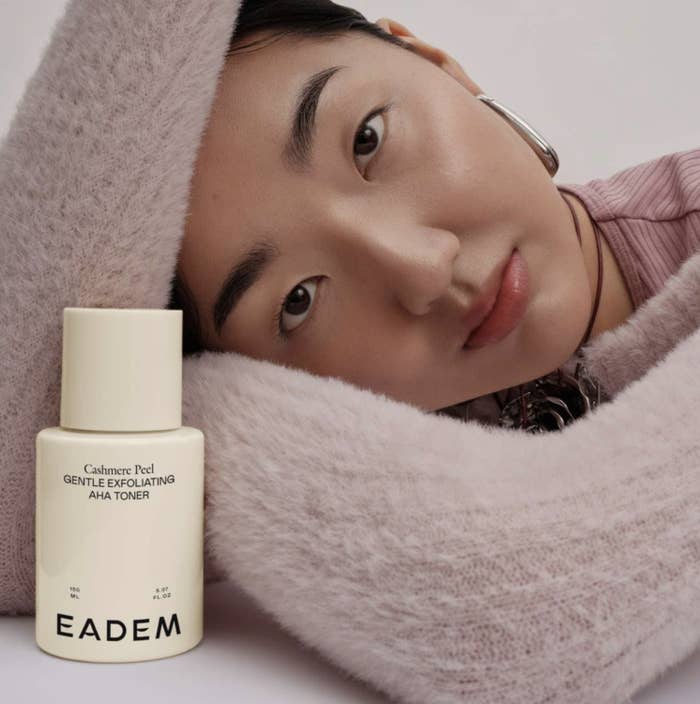 person wearing a plush sweater and posing with EADEM skincare product