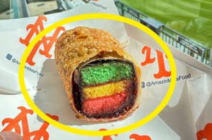 Hand holding a rainbow-layered pastry at a sports stadium