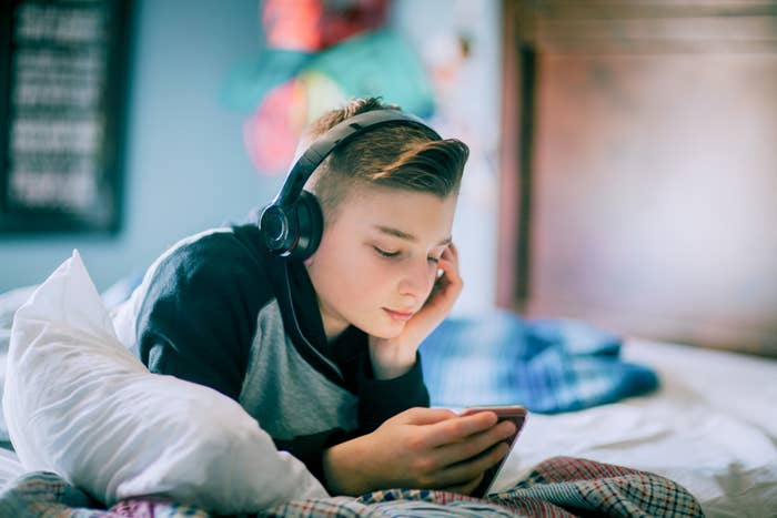 Teenager with headphones lying on bed using smartphone