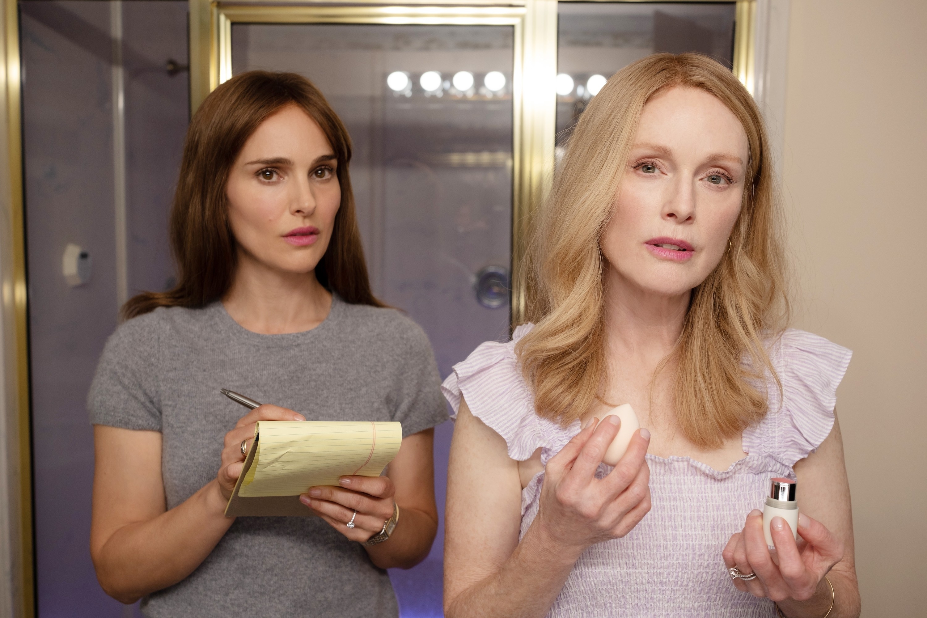 Julianne Moore and Natalie Portman in a dressing room, Natalie holding a notepad, Julianne with makeup, in May December