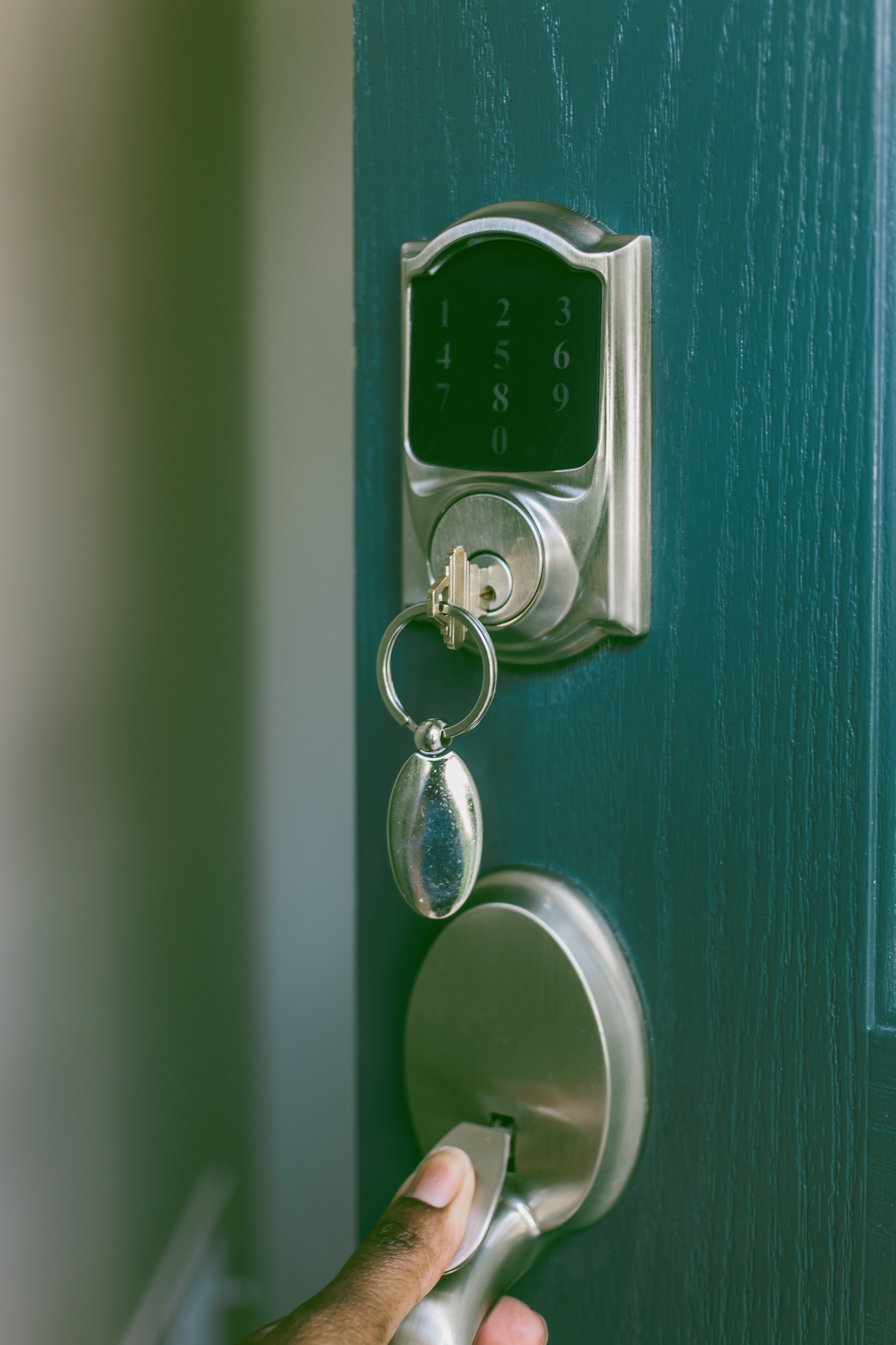 Person&#x27;s hand using a keyless entry pad with a keychain hanging from the knob