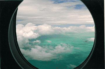 Vista de nubes y mar turquesa desde la ventana de un avión, que evoca la experiencia de viajar
