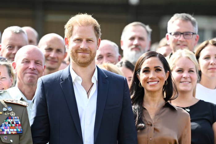 Prince Harry and Meghan Markle posing with a group, Meghan in a button-up shirt