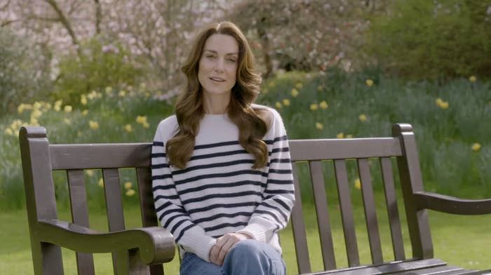 Kate in a striped sweater sitting on a bench with greenery and flowers in the background