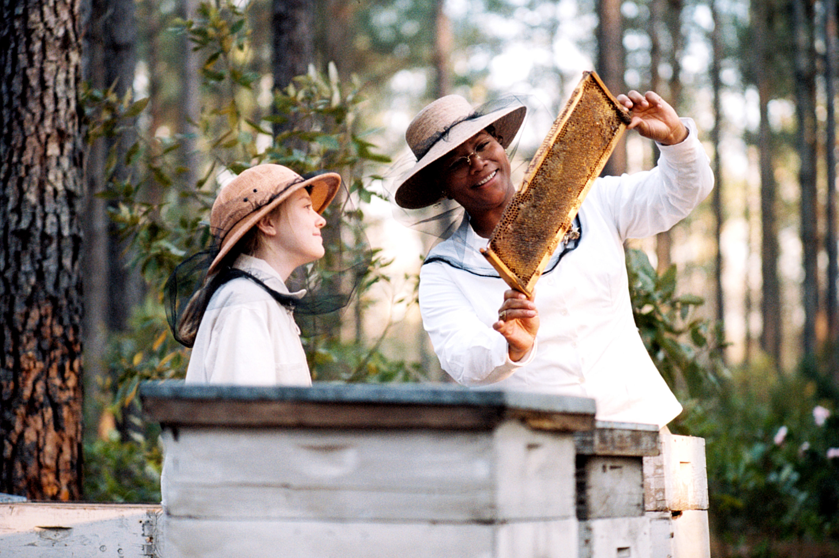 Two people in beekeeping suits inspect a honeycomb frame outdoors